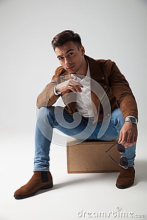 Young casual man sitting on a box and holds sunglasses Stock Photo