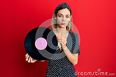 Young caucasian blonde woman holding vinyl disc relaxed with serious expression on face Stock Photo