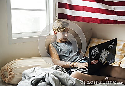 Young caucasian boy lying using computer laptop on bed Stock Photo