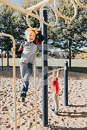 Young Caucasian boys friends hanging on monkey bars and pull-up bars in park on playground. Summer outdoor activity for kids. Stock Photo