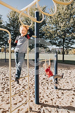 Young Caucasian boys friends hanging on monkey bars and pull-up bars in park on playground. Summer outdoors activity for kids. Stock Photo