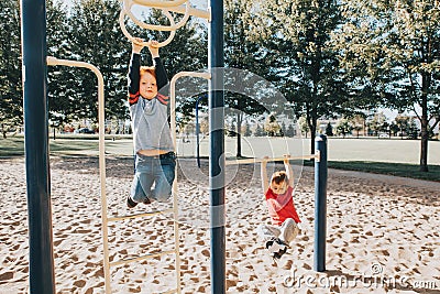Young Caucasian boys friends hanging on monkey bars and pull-up bars in park on playground. Summer outdoors activity for kids. Stock Photo