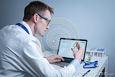 Young caucasian doctor working at table in hospital laboratory examining an ampoule of medicine and entering data into Stock Photo