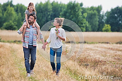 Young Caucasian family walking across field with young girl holding bouquet of flowers, concept organic ecologically friendly fami Stock Photo