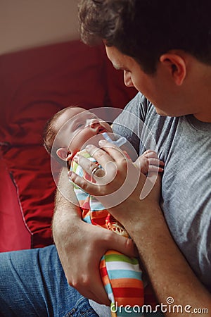 Young Caucasian father trying to calm down newborn baby. Male man parent holding rocking child on his hands Stock Photo