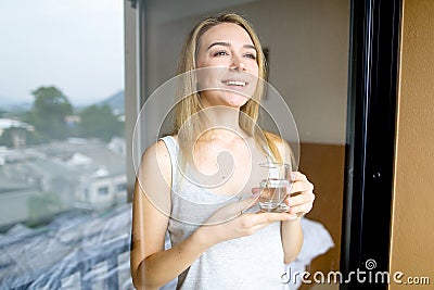 Young caucasian female person drinking glass of water in morning at hotel. Stock Photo