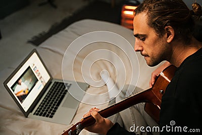 Young caucasian male learning guitar online with laptop Stock Photo