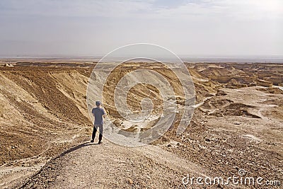 Young caucasian man in baseball cap staying alone in desert and looking ahead to the horizon. Young traveller discovering lifeless Editorial Stock Photo