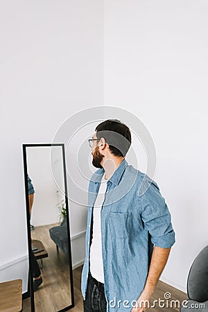 Young caucasian man in glasses standing at the mirror in living room Stock Photo