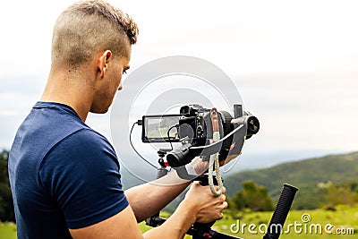 Young caucasian man handling a camera on top of a gimbal while working on recording a scene Stock Photo