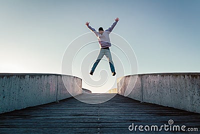 Young caucasian man in jeans and hoodie jumping with spread out arms on concrete bridge. Mid air parkour pose in city environment Stock Photo