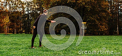 Young caucasian man playing disc golf on autumn play course with basket Stock Photo