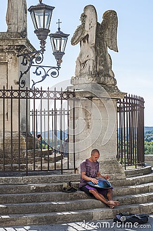 Young Caucasian man plays hang drum on the stairs to an angel statue in Avignon, France Editorial Stock Photo