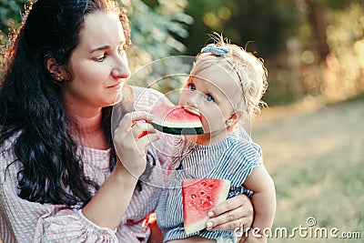 Young Caucasian mother with baby girl eating watermelon. Healthy finger food for babies. Summer sweet fruit food snack. Stock Photo