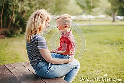 Young Caucasian mother and boy toddler son sitting together face to face. Family mom and child talking communicating outdoor on a Stock Photo