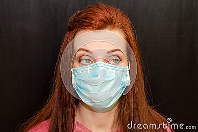 Young crazy tired redhaired girl with green eyes in medical mask, pink sweater on black background, coronavirus epidemic Stock Photo