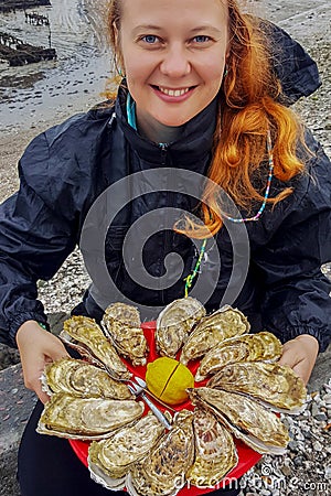 Young Caucasian white woman with red hair holds in her hands a plate with oysters and lemon Stock Photo