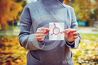 Young Caucasian woman in autumn park showing piece of paper with transgender symbol drawn in it. Human rights day concept. Stock Photo