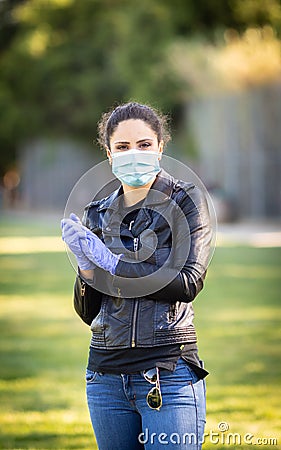 Young Caucasian woman in black leather jacket and surgical mask takes on purple latex gloves Stock Photo