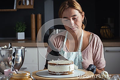 Young caucasian woman decorating cake with professional tools. Confectioner in the modern stylish kitchen Stock Photo