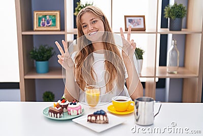 Young caucasian woman eating pastries t for breakfast smiling looking to the camera showing fingers doing victory sign Stock Photo