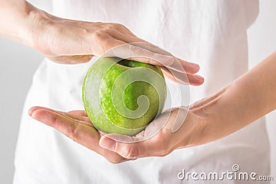 Young Caucasian woman girl in white shirt holding in hands raw green organic apple. Stomach gut health dietary fiber for digestion Stock Photo