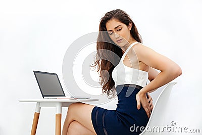 Young Caucasian woman having chronic back pain / backache / office syndrome while working with laptop on white desk Stock Photo