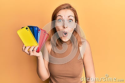 Young caucasian woman holding smartphone case scared and amazed with open mouth for surprise, disbelief face Stock Photo
