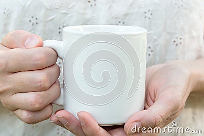 Young caucasian woman holding a white mug, mock up, blank space for text, artwork, hands, linen shirt Stock Photo