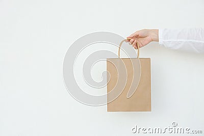 Young caucasian woman holds in hand empty blank mock up brown craft paper bag on white wall background. Christmas New Years Stock Photo