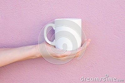 Young Caucasian Woman Holds on Hand Palm Blank Mockup White Mug on Light Pink Painted Wall. Airy Breezy Style Stock Photo