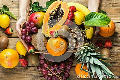 Young caucasian woman holds in hands box with raw organic tropical and seasonal summer fruits berries. Halved papaya coconut mango Stock Photo