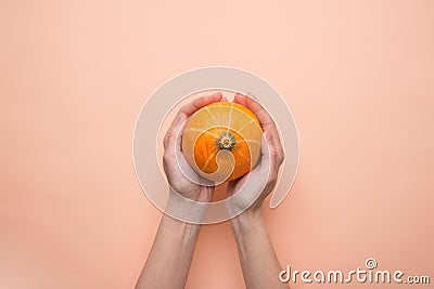 Young Caucasian Woman Holds in Hands Small Round Heirloom Orange Pumpkin on Peachy Pink Background. Fall Autumn Stock Photo