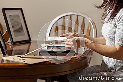 A young caucasian woman is placing a printed photograph into a picture frame with kickstand. Stock Photo