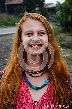 A young Caucasian woman with red hair chews traditional Asian tobacco - betel leaves, which makes her mouth bright red. Stock Photo