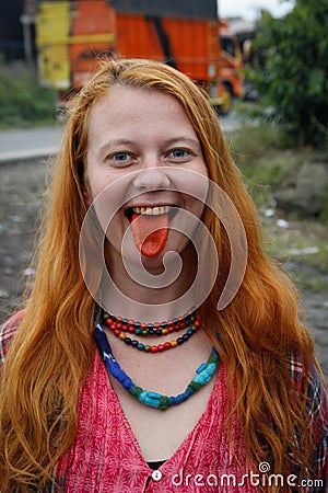 A young Caucasian woman with red hair chews traditional Asian tobacco - betel leaves, which makes her mouth bright red. Stock Photo