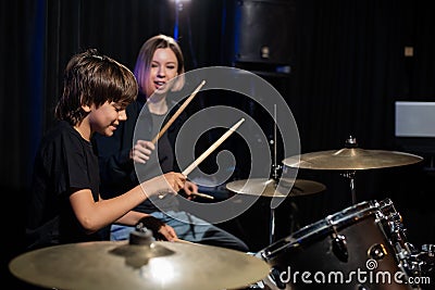 Young caucasian woman teaches a boy to play the drums in the studio on a black background. Music school student Stock Photo