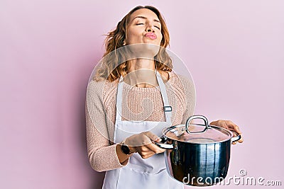 Young caucasian woman wearing apron holding cooking pot looking at the camera blowing a kiss being lovely and sexy Stock Photo