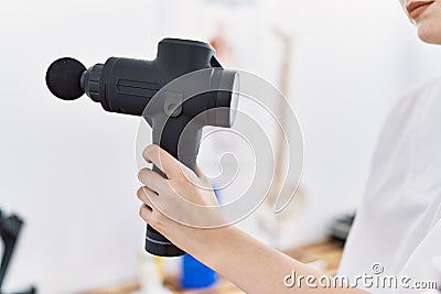 Young caucasian woman wearing physio therapist uniform using percussion pistol at clinic Stock Photo