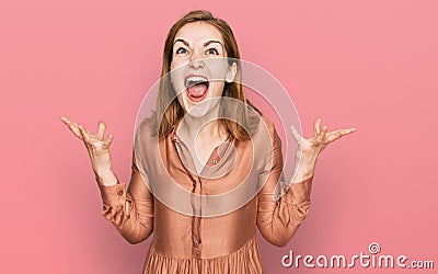 Young caucasian woman wearing sexy party dress crazy and mad shouting and yelling with aggressive expression and arms raised Stock Photo