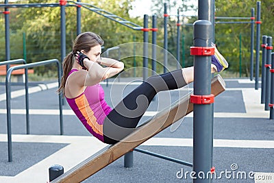 Young caucasian woman workouts on the park sports ground. The girl does abdominal excersise, in black and lilac sportswear. White Stock Photo