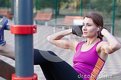 Young caucasian woman workouts on the park sports ground. The girl does abdominal excersise, in black and lilac sportswear. White Stock Photo