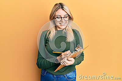 Young caucasian woman writing on checklist clipboard smiling with a happy and cool smile on face Stock Photo