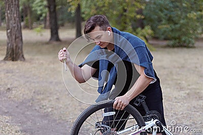 Young causacian man with screwdriver tries to damage the bicycle wire at the abandoned park. Vandal actions. Stock Photo