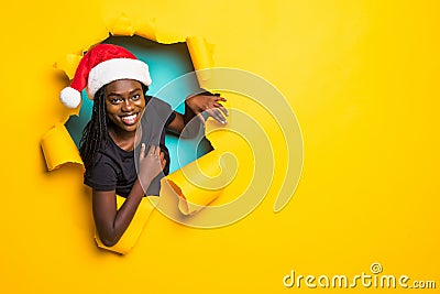 Young charming african woman wear in santa hat standing in yellow torn paper hole background Stock Photo