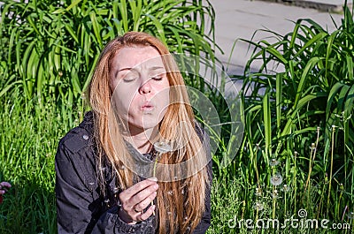 Young charming beautiful girl with long hair Europeans in a meadow with grass and flowers, plucked a flower dandelion and blowing Stock Photo
