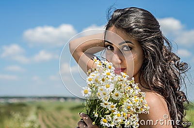 Young charming brunette girl with a bouquet of white field chamomiles on a summer sunny day Stock Photo