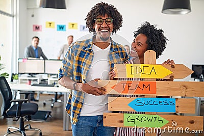 Young cheerful colleagues are enjoying posing for a photo while promoting company slogans in the office. Employees, job, office Stock Photo