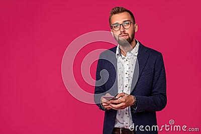 Young cheerful lawyer or businessman is standing on the pink background and smiling, reading good news on internet at Stock Photo