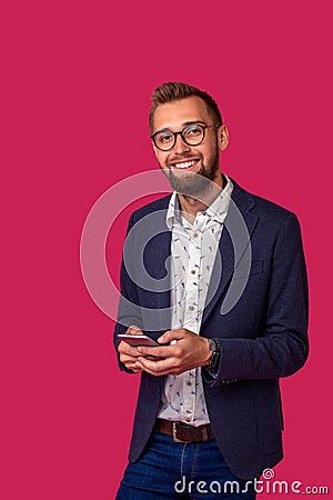 Young cheerful lawyer or businessman is standing on the pink background and smiling, reading good news on internet at Stock Photo